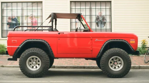 Film photo of a classic red Ford Bronco parked on a street in front of storefront windows.