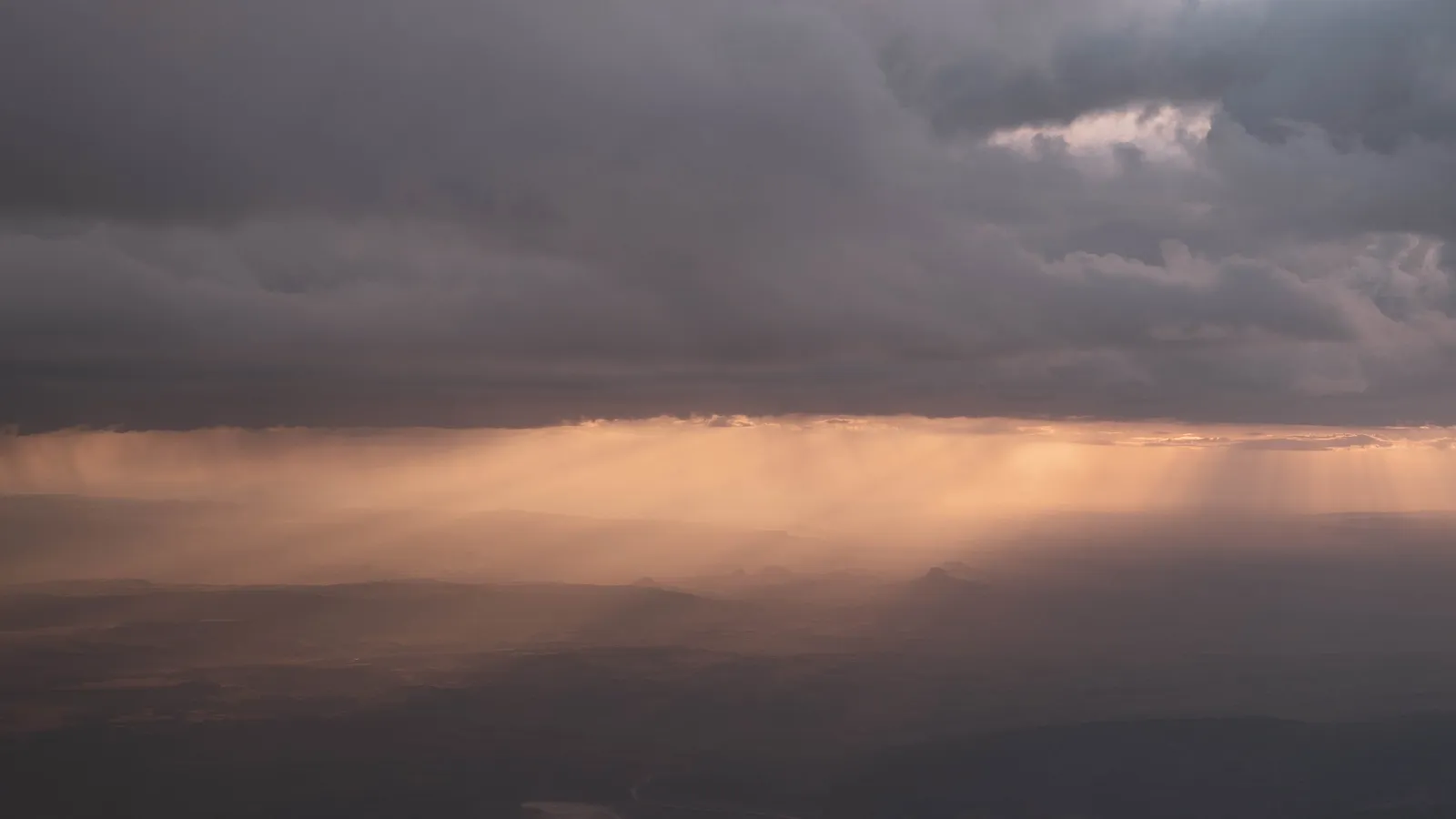 Storm clouds over a mountain valley at sunset, shafts of golden light breaking through onto distant peaks.