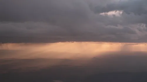 Storm clouds over a mountain valley at sunset, shafts of golden light breaking through onto distant peaks.