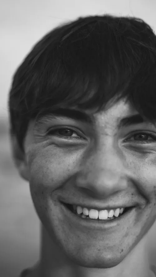 Close-up black-and-white portrait of a young man laughing, looking directly at the camera.