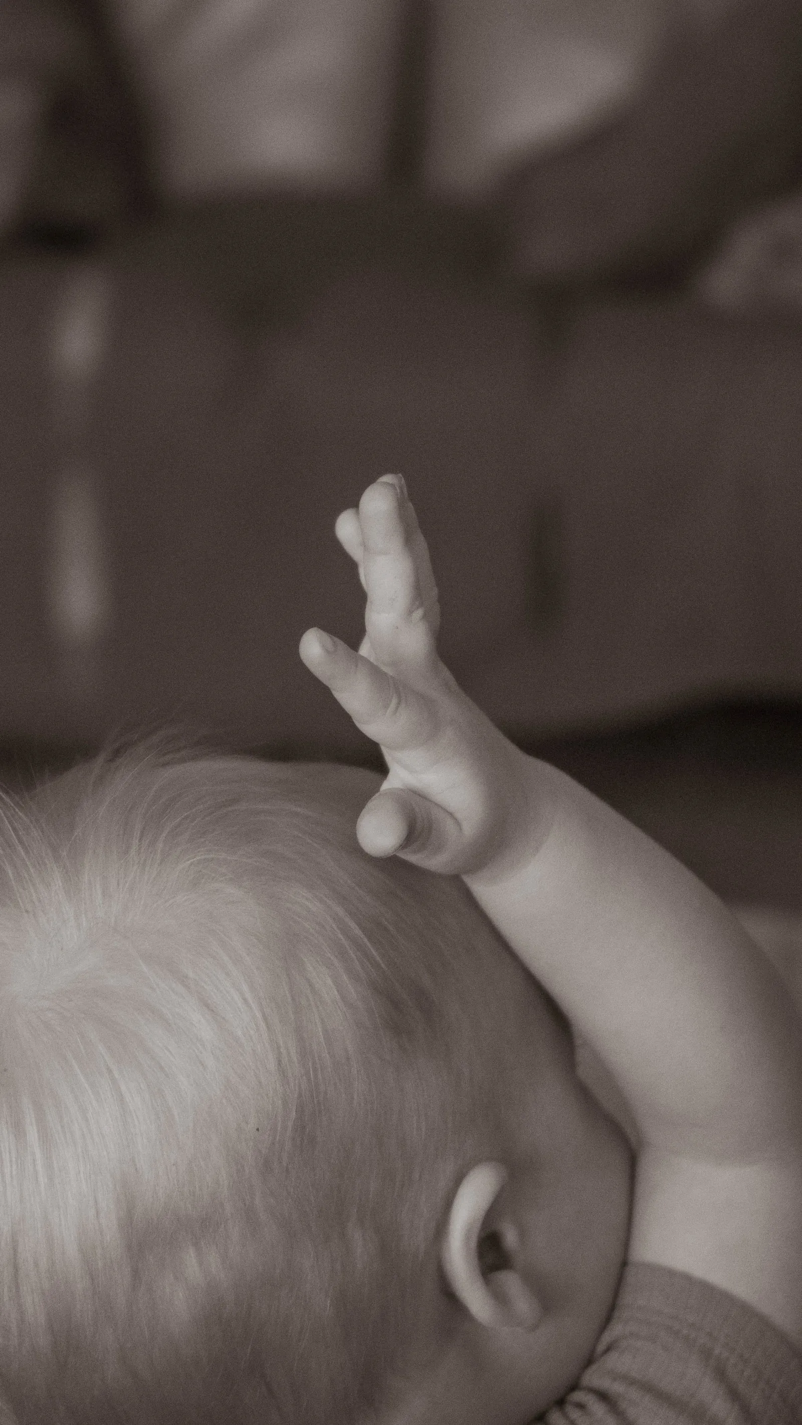 Sepia close-up of a baby's raised hand and the top of their head.