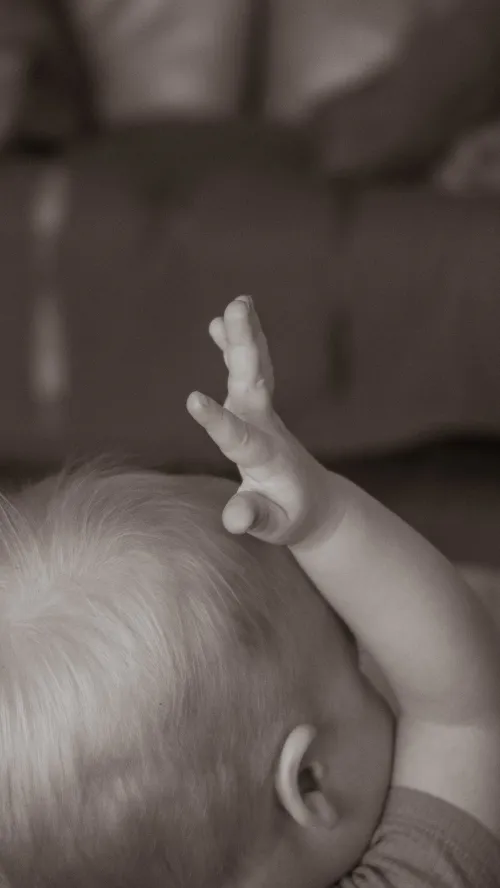 Sepia close-up of a baby's raised hand and the top of their head.