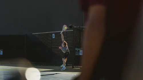 A Bates College tennis player leaping into an overhead serve on an outdoor court.