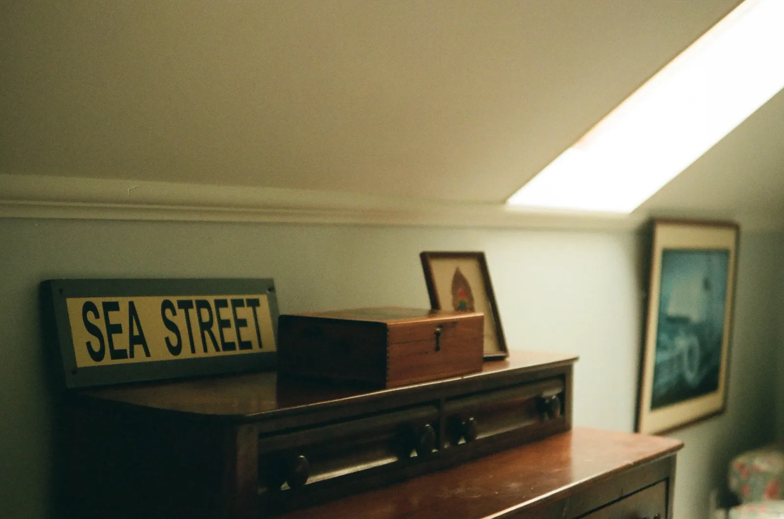 Film photo of a "Sea Street" sign, a wooden box, and framed pictures on top of an antique dresser.