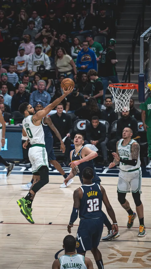Boston Celtics forward Jayson Tatum driving to the basket for a layup past Denver Nuggets defenders.