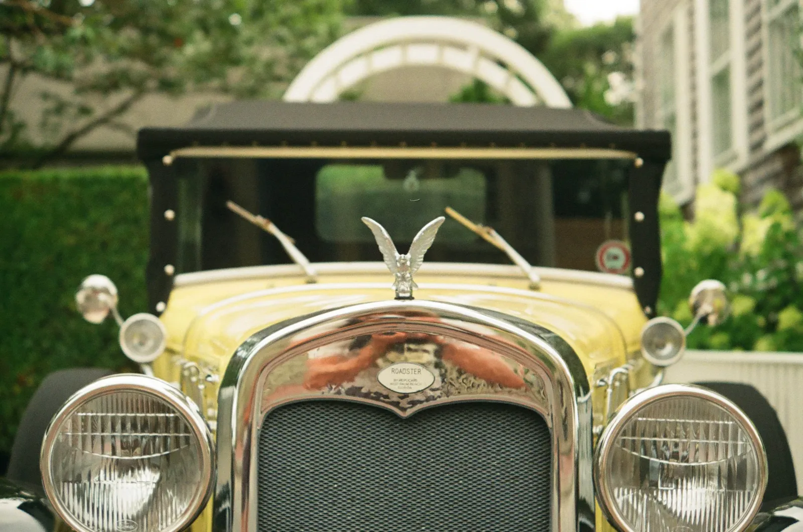 Film photo close-up of the front grille and hood ornament of a vintage yellow roadster.