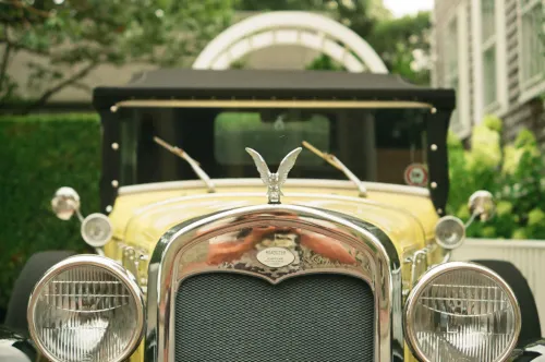Film photo close-up of the front grille and hood ornament of a vintage yellow roadster.