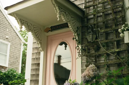 Film photo of a Nantucket-style shingled house entrance with a pink oval-windowed door and house number 56.