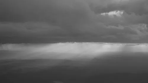 Black-and-white view of a band of rain falling from storm clouds over a distant mesa landscape.