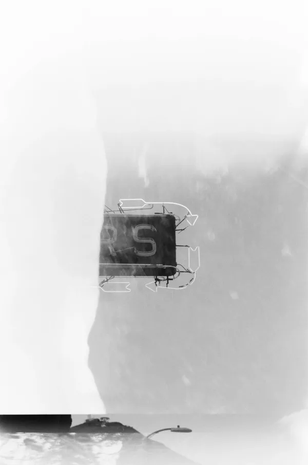 Double-exposed film photo overlaying a neon sign reading "RS" with a hazy mountain landscape.